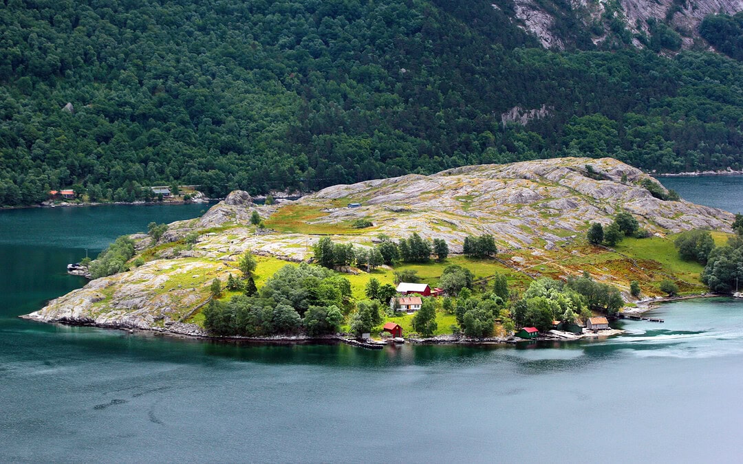 Secluded island with lush greenery, rocky terrain, and scenic fjord views in Norway.