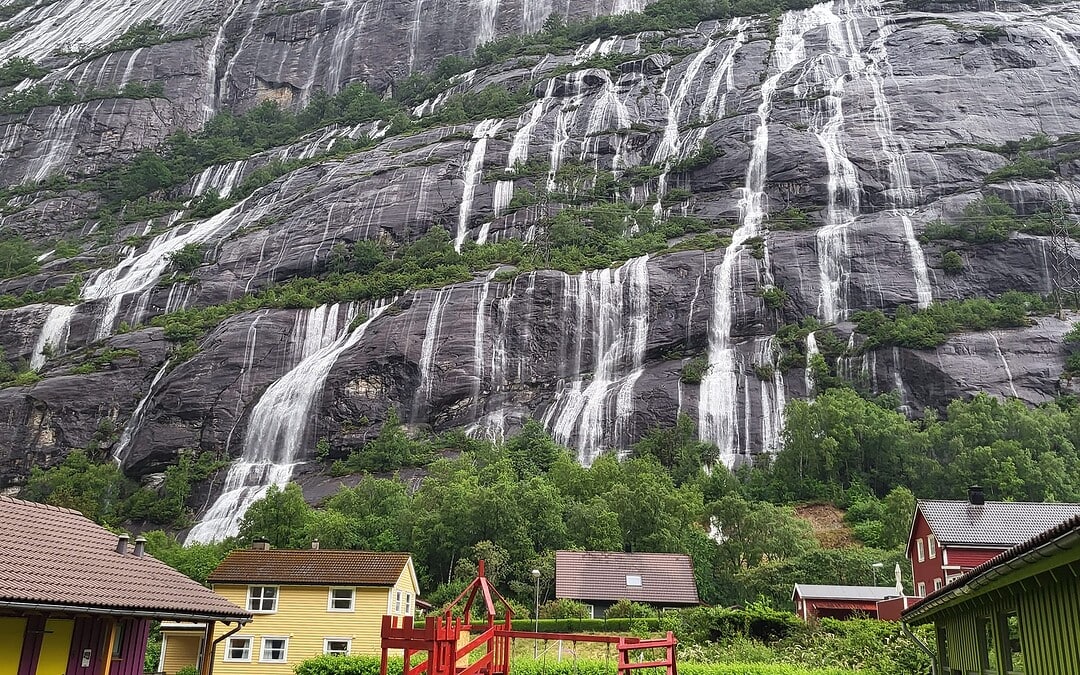 Sheer Kjerag mountain with waterfalls cascading down, viewed from a small village at its base in Lysefjord, Norway.