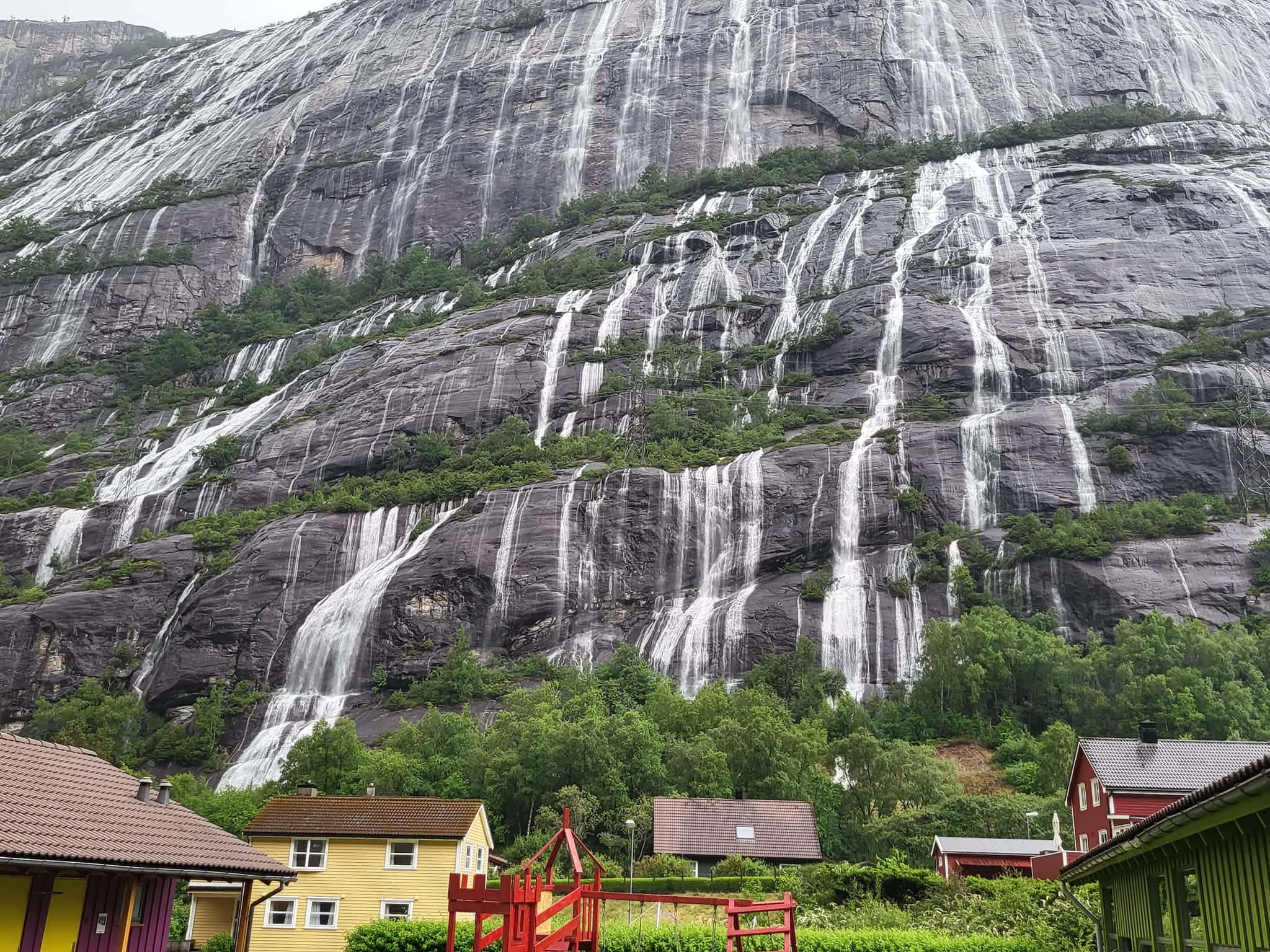 Sheer Kjerag mountain with waterfalls cascading down, viewed from a small village at its base in Lysefjord, Norway.